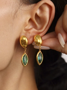 Vue rapprochée des boucles d'oreilles dorées avec cristal vert montrant les détails de luxe