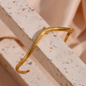 Detailed view of wave-shaped golden stainless steel open cuff bracelet on stone
