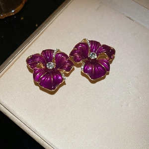 Détail de boucles d'oreilles fleurs en émail violet avec bordure dorée et zircon cubique