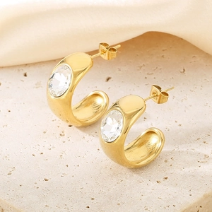 Detailed close-up of C-shaped gold-plated earrings with clear crystal on stone surface