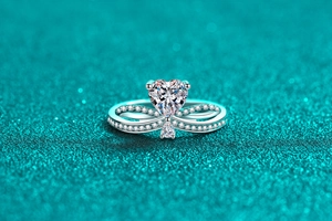 Macro shot of a heart-shaped moissanite ring with infinity pavé silver band on teal glitter