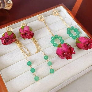 Detailansicht langer Perlenohrringe mit roten Rosen, grünen Perlen und Goldketten