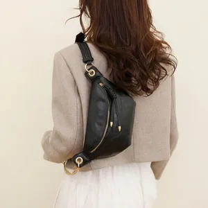 Détail du sac de poitrine en cuir noir avec zip doré porté sur un tailleur beige