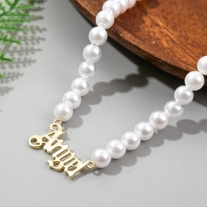 Close-up of golden Angel script pendant on a multi-layer white baroque pearl necklace