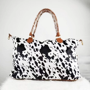 Detail of cow print weekender bag featuring brown leather handles and canvas texture