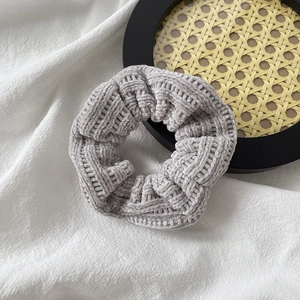 Detailed view of light gray knitted scrunchie with soft ribbed plush texture on linen