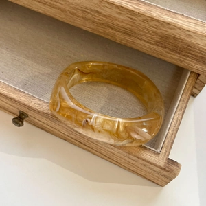 Close-up of amber marble resin bangle with translucent texture in a vintage wooden drawer