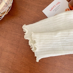Detailed macro view of white knitted leg warmer with wavy ruffle hem and ribbed texture