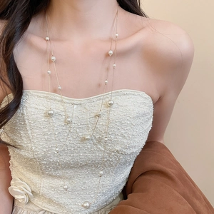 Detailed close-up of double-layer pearl necklace with golden chain on a white dress