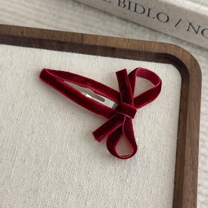 Macro view of burgundy velvet bow hair clip with metal base on beige fabric tray
