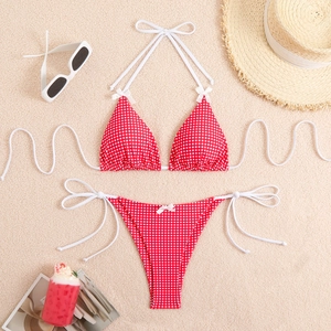 Flat lay of red gingham bikini set with straw hat and sunglasses on a sandy background