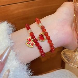 Détail de bracelets en perles d'agate rouge avec breloques de cheval dorées sous lumière