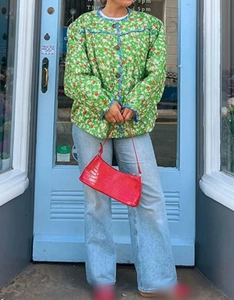 Detail view of women's green floral quilted jacket with blue contrast trim and red bag