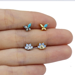 Macro shot of silver butterfly and golden paw cartilage studs with opal and turquoise stones