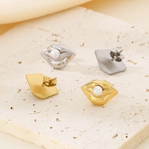 Gold and silver lip-shaped stud earrings with pearls on a minimalist stone surface