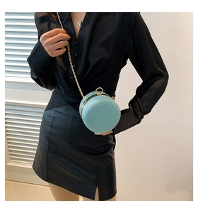 Petit sac rond bleu pailleté avec chaîne dorée porté sur une tenue noire
