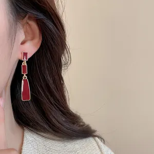 Detail of red geometric drop earrings with gold edges worn by a model in soft light
