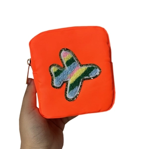 Hand holding orange nylon makeup bag with airplane patch and gold zipper on white background