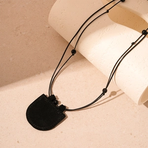 Detail of a minimalist black faux leather pouch pendant on a woven cord necklace