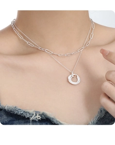 Detail of layered silver necklace with paperclip chain and orange gemstone ring pendant