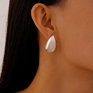 Gros plan d'une boucle d'oreille goutte argentée mate portée sur le lobe d'oreille