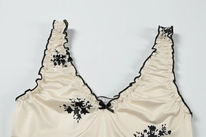 Close-up of V-neck floral satin dress featuring black ruffle trim and bow detail