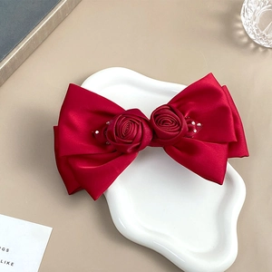 Close-up of red satin bow hair clip with handmade roses and rhinestone tassel details
