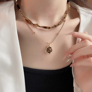 Detail of layered gold-plated necklace with tiger eye stone beads and a round pendant