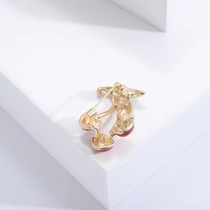 Detailed view of cherry brooch with red enamel glaze and golden finish on white background
