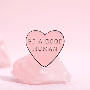 Detailed view of pink heart enamel pin with 'BE A GOOD HUMAN' text on crystal