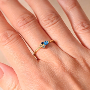 Macro shot of a thin gold ring featuring blue and white zircon stones worn on a finger