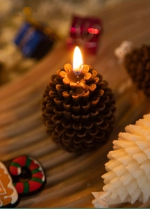 Close-up of a burning pine cone shaped candle with warm holiday glow and festive bokeh