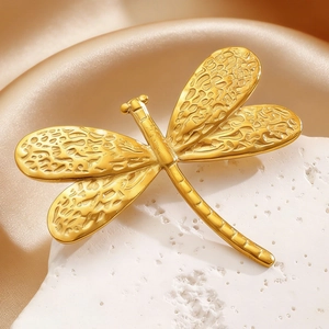 Macro view of a golden dragonfly brooch with detailed textured wings on white stone