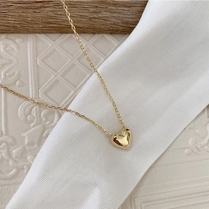 Detail of 18K gold heart pendant on thin chain over white silk and vintage relief