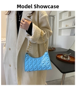 Close-up of light blue quilted underarm bag with thick gold chain strap on shoulder