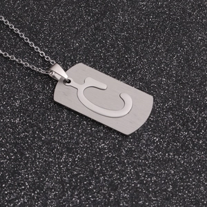 Gros plan d'un pendentif rectangulaire en acier argenté avec lettre C évidée sur fond noir