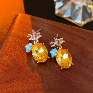 Gros plan sur des boucles d'oreilles ananas en argent avec pierres jaunes et bleues