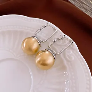 Modern geometric square earrings with matte gold spherical charms on white ceramic