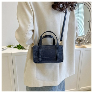 Detail shot of navy blue crocodile pattern leather texture and gold hardware on bag