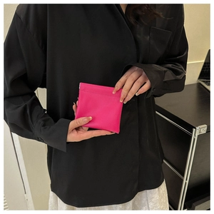 Close-up of a fuchsia mini leather coin purse held by a model in a black shirt