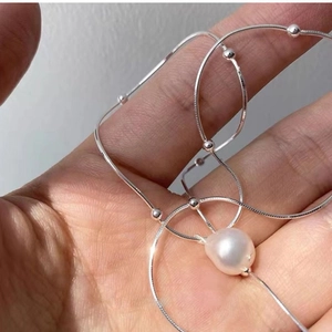 Close-up of irregular pearl pendant on silver snake chain held in person's hand