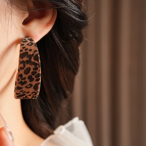 Close-up of a C-shaped leopard print earring with a soft velvet texture on model