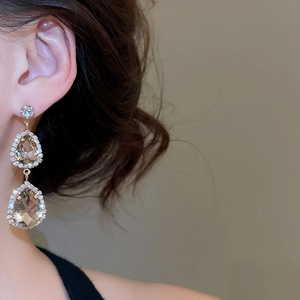 Close-up of champagne teardrop crystal earrings in rose gold worn on a female model
