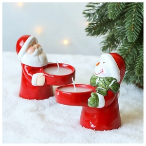 Close-up of Santa and Snowman ceramic candle holders on snow with pine branch
