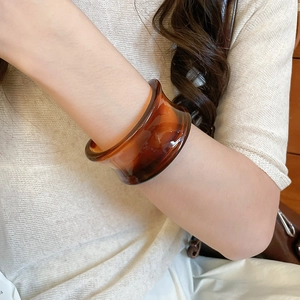 Close-up of a wide amber resin bangle with a vintage tortoiseshell pattern on a model's wrist