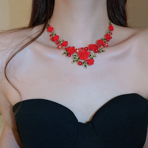 Detail of a floral necklace featuring 3D red roses, green leaves, and golden chains