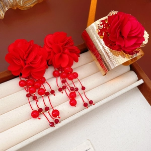 Détail de boucles d'oreilles fleurs rouges à franges et bracelet manchette doré assorti