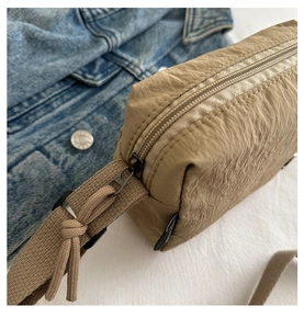 Close-up of smooth khaki nylon crossbody bag zipper with decorative woven cord puller