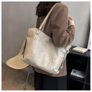 Close-up of beige PU leather tote bag with gold hardware worn by a model in a minimalist room