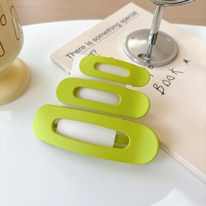 Close-up of vibrant lime green matte hair clip with triple oval cutout design on a desk